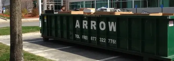 Green yard waste dumpster from Arrow Container Services, parked in a commercial area, displaying contact information and branding.