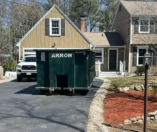 Green dumpster from Arrow Container Services placed in residential driveway, with house in background and delivery truck visible, illustrating efficient waste management solutions for home projects.